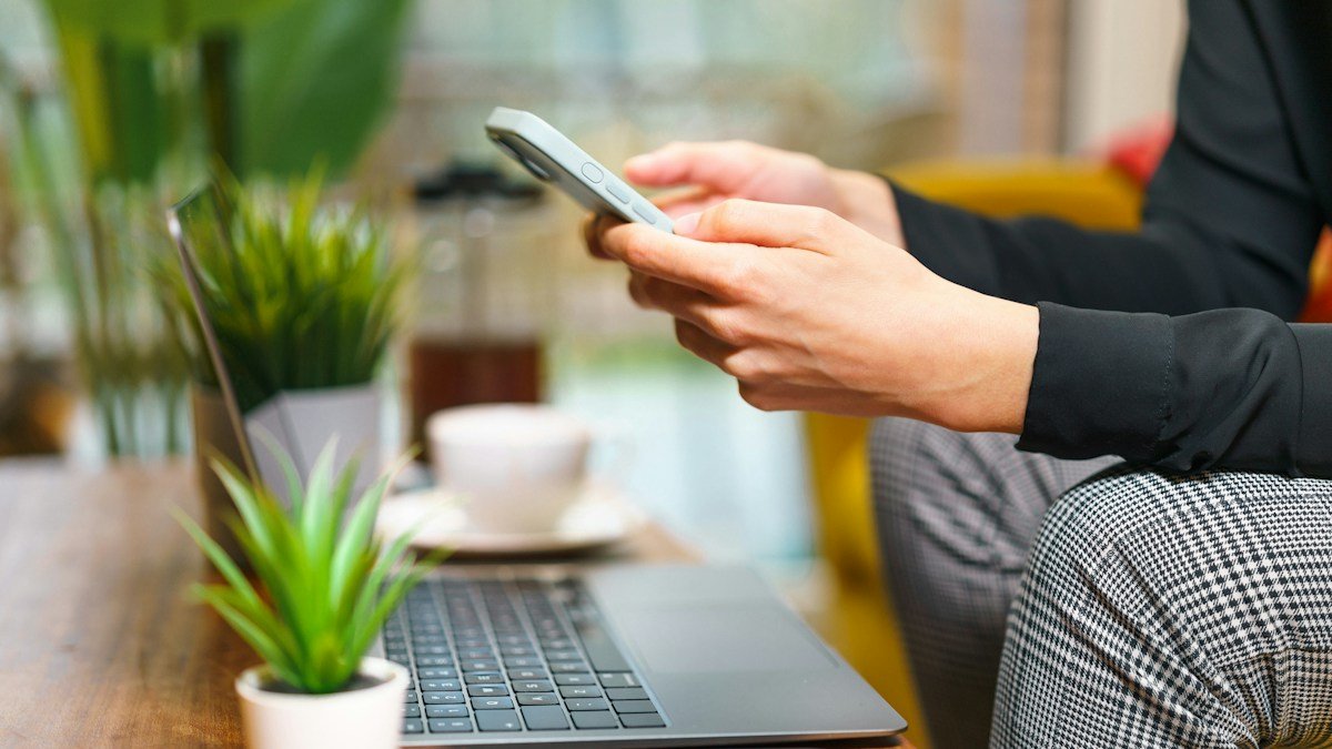 Mains tenant un smartphone à côté d'un ordinateur portable ouvert et d'une tasse de café