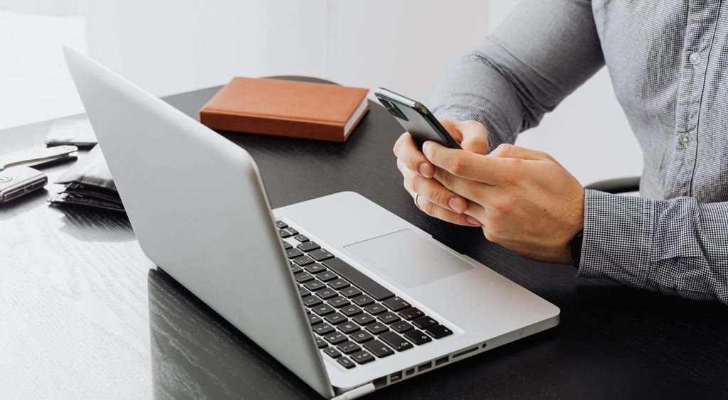 Person setting up a smartphone while sitting at a desk beside a laptop