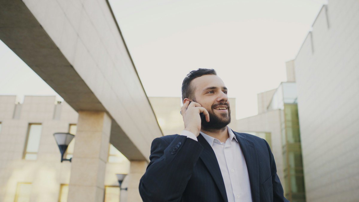 Man in a blazer smiling during a mobile phone call outside a modern building