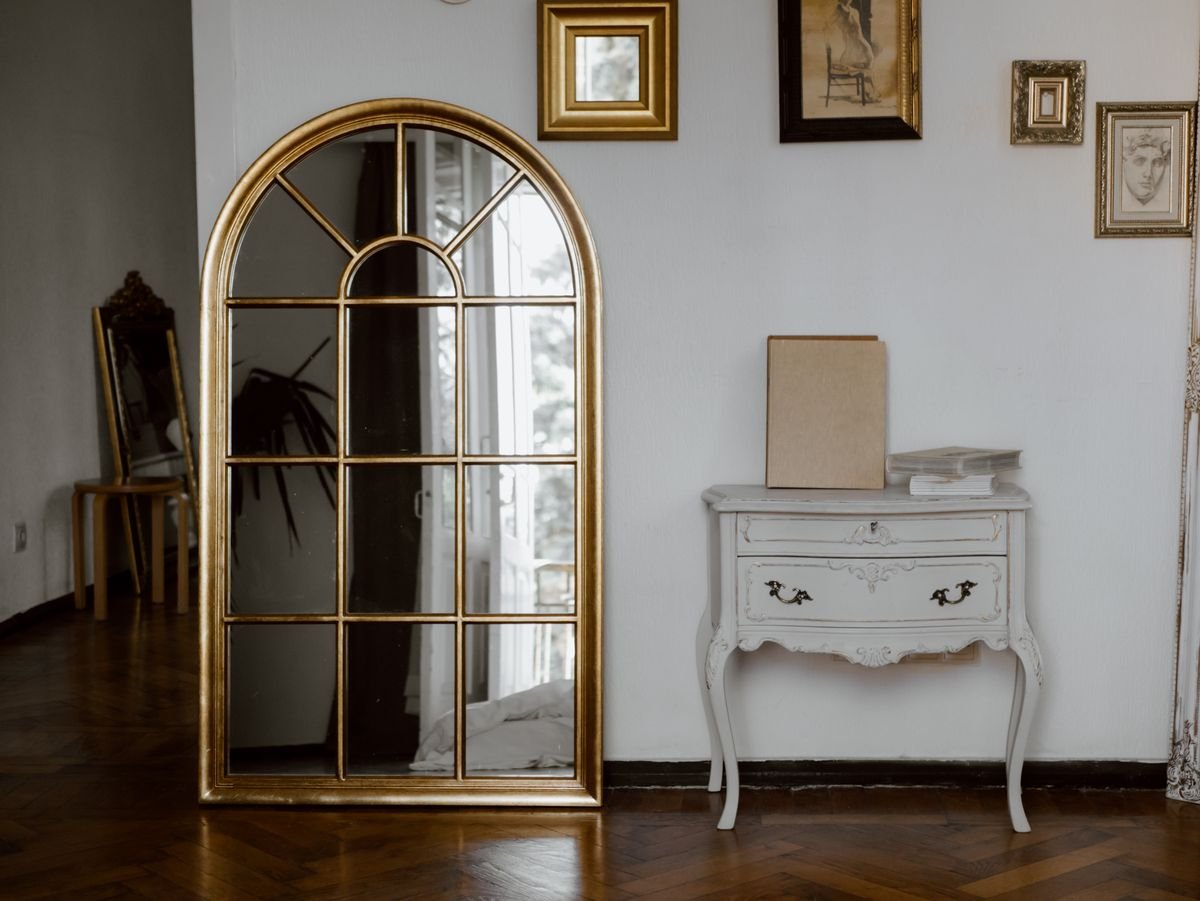 Gold arched mirror leaning against a wall beside a white console