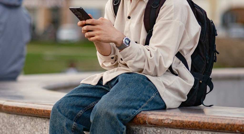 Person mit Rucksack schaut auf ihr Handy