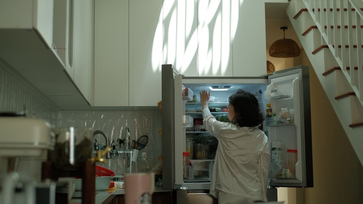 Woman reaching into an open refrigerator with full shelves at home