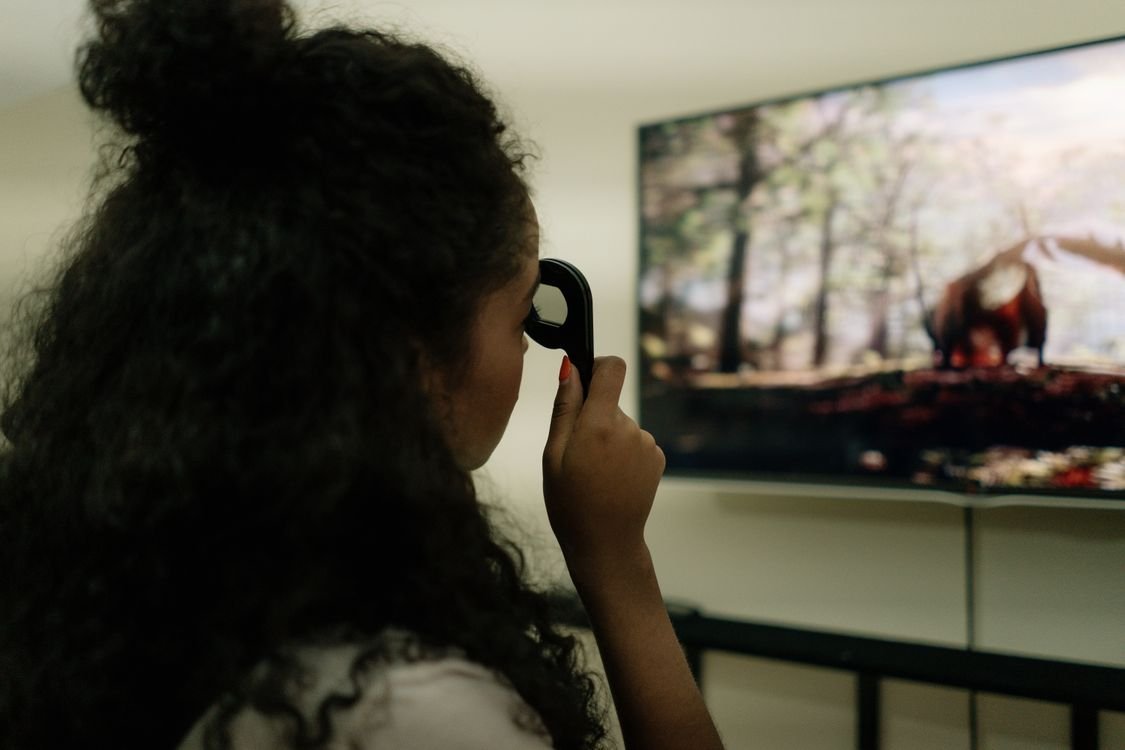 Woman holding a remote in front of a large television showing a nature scene