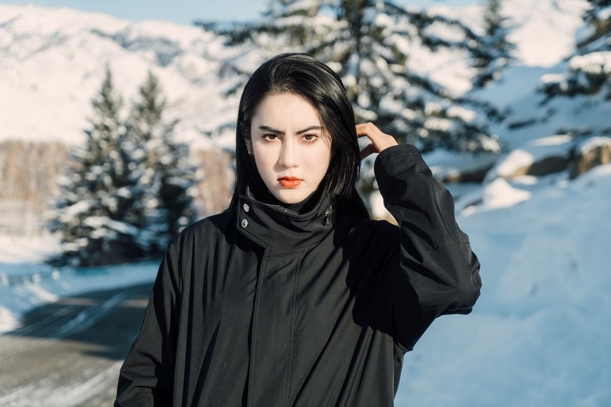 Frau in schwarzer Winterjacke vor verschneiten Tannen